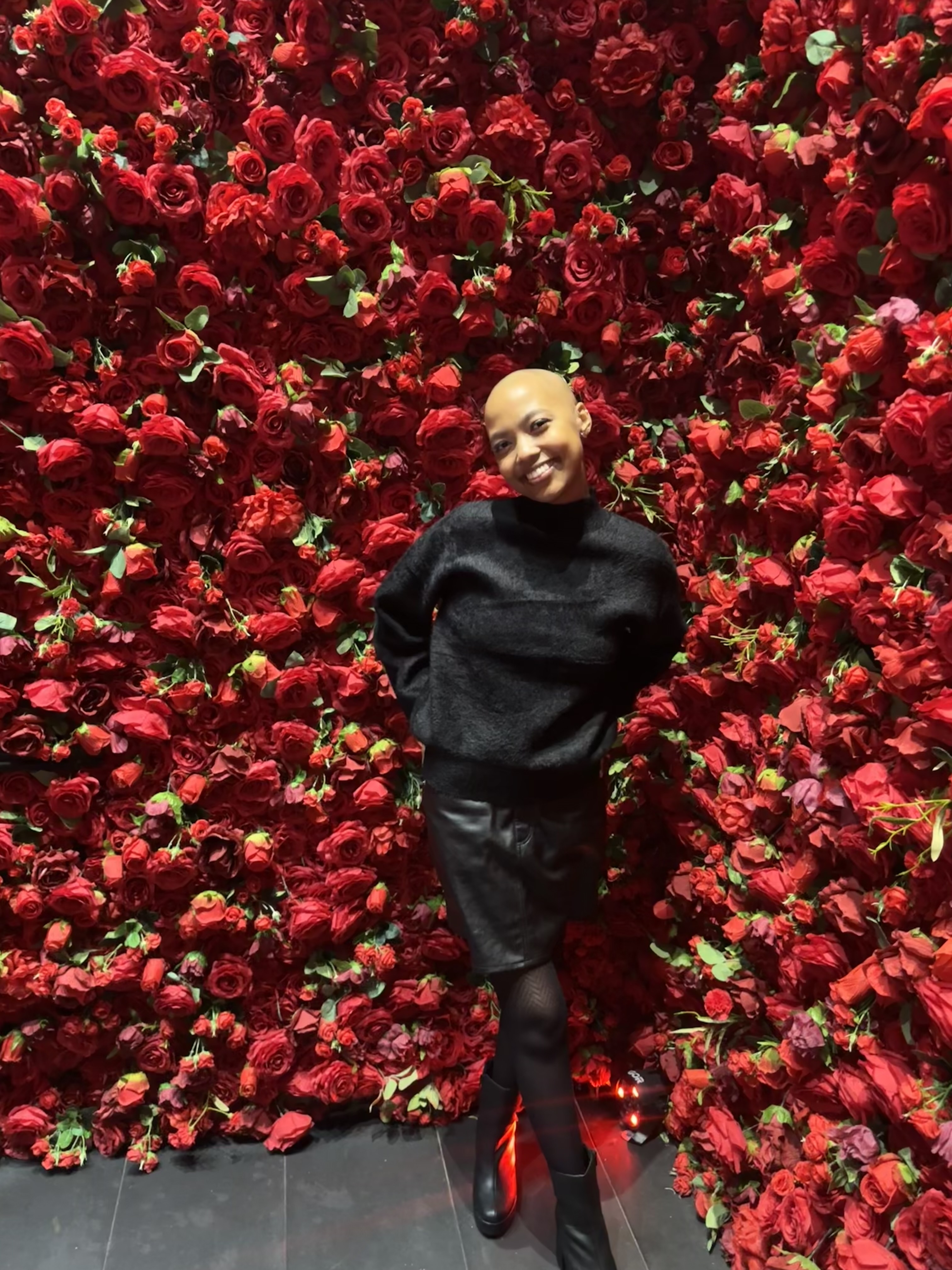 young black woman, bald, dressed in black in front of red roses