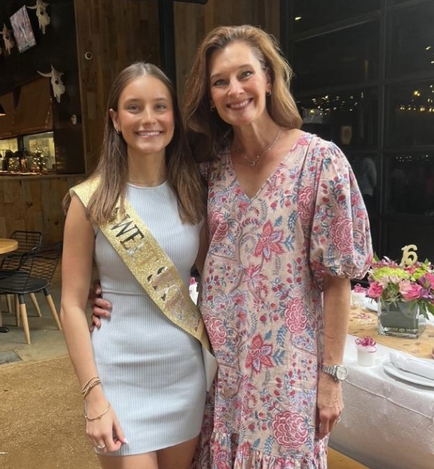 young white woman wearing sweet sixteen sash and white dress with cowboy boots and her mother in a floral dress and sneakers