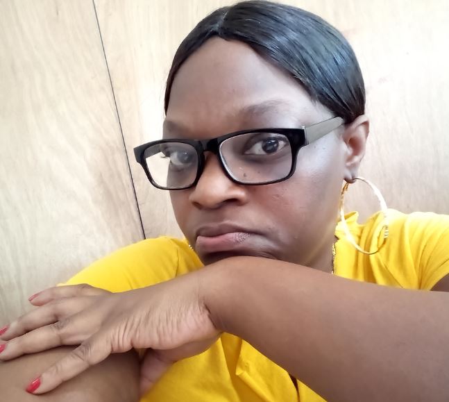 black woman with her hair pulled back wearing black glasses and a yellow shirt resting her chin on her arm