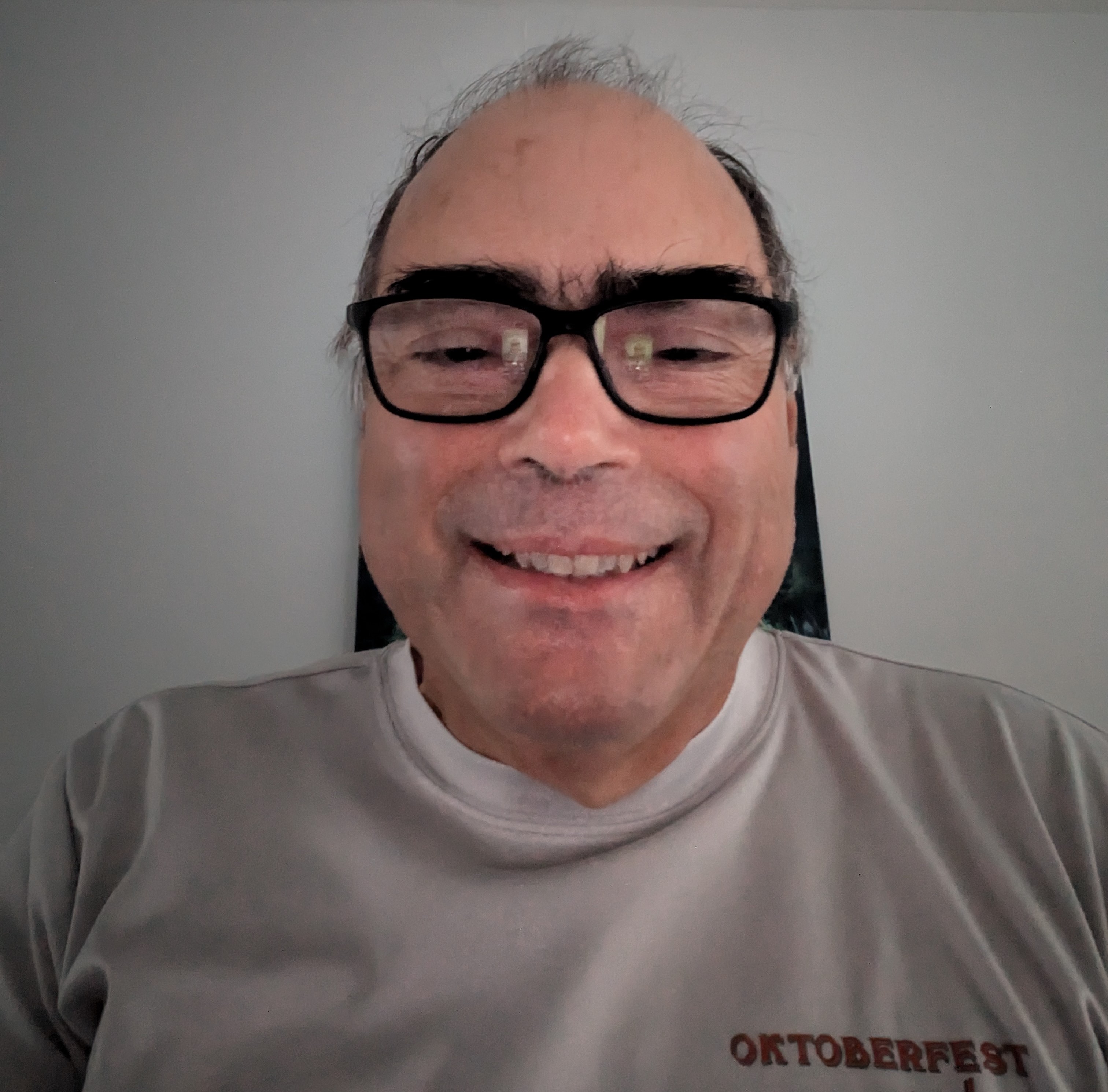 middle aged balding hispanic man with bushy eyebrows wearing black glasses and an Oktoberfest t-shirt