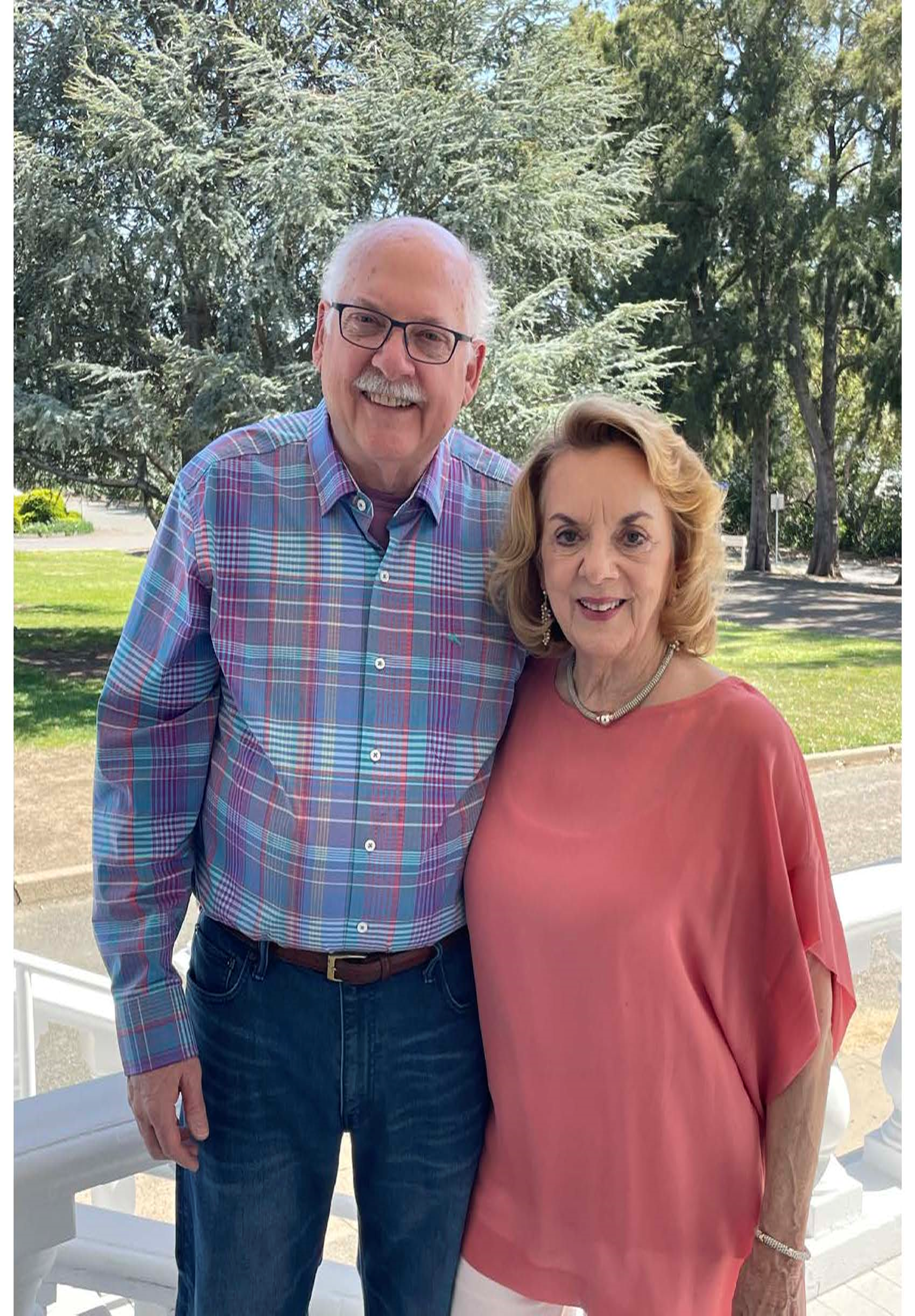 older white balding man with glasses and blue plaid shirt with older white woman with blond hair necklace and pink blouse