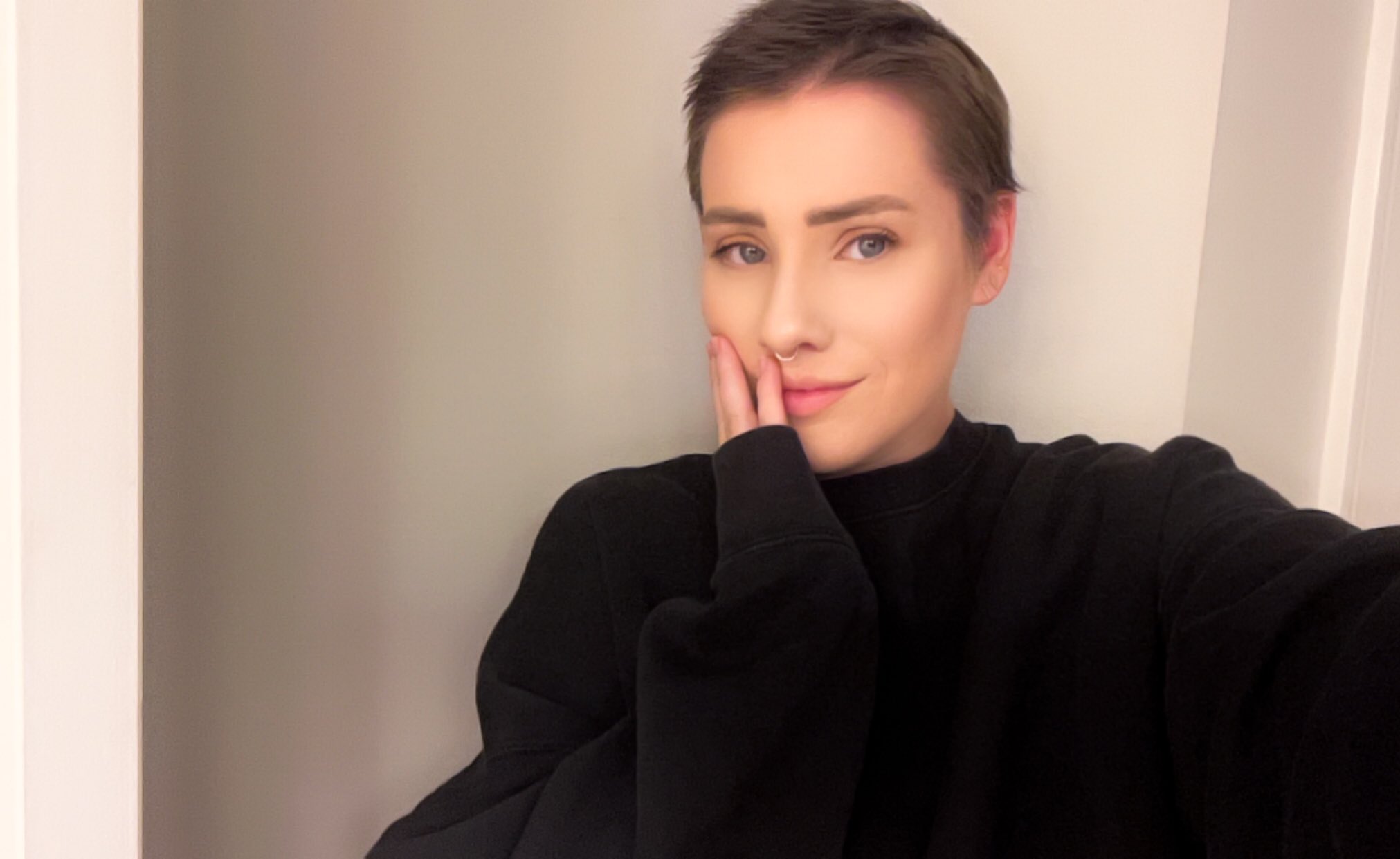 young white woman with short hair and a nose ring wearing a black sweater hand on her face