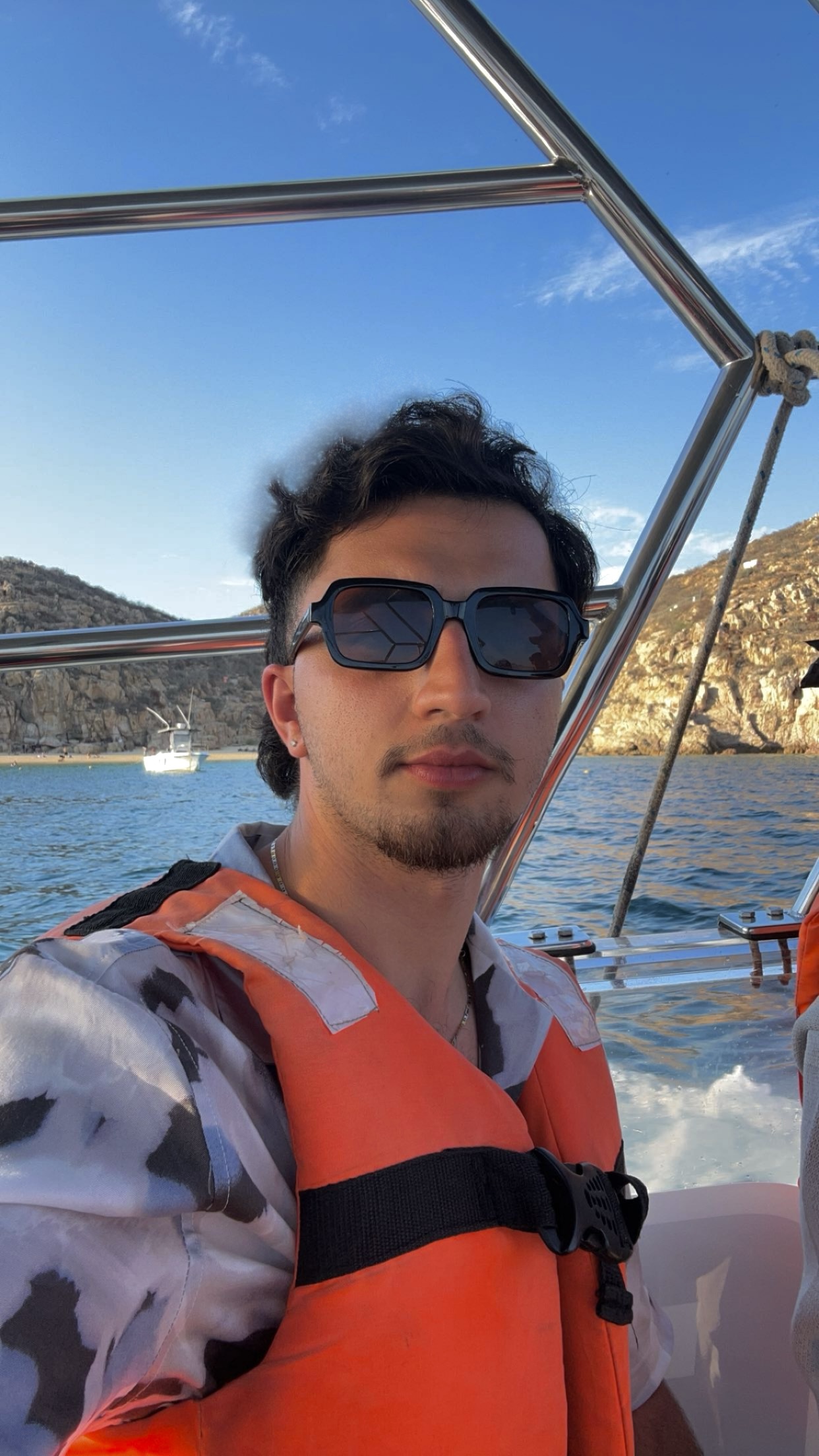 Steven young white male with dark hair and light mustache and beard wearing sunglasses and life vest over white and black shirt standing on a boat