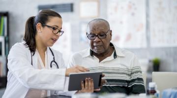 Doctor in white lab coat looking at tablet with patient